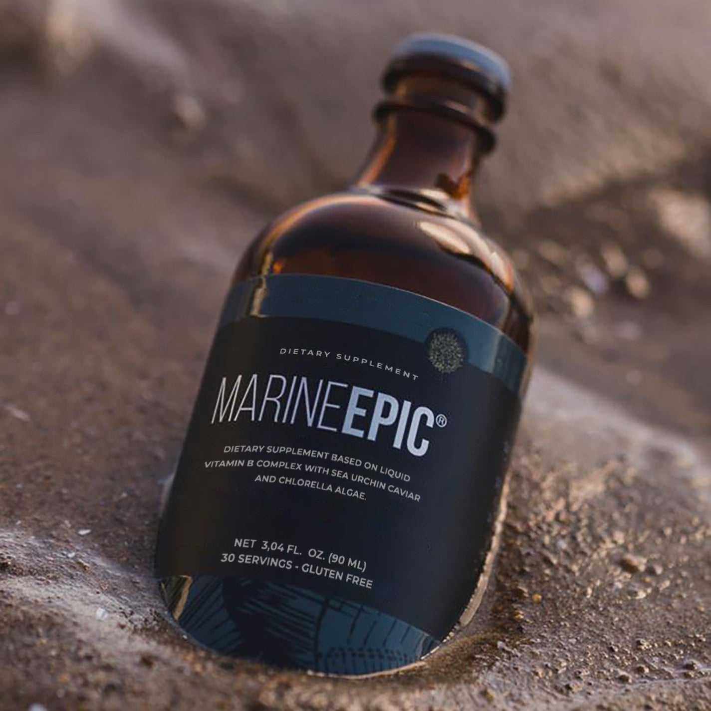 Marine Epic dietary supplement bottle featuring liquid vitamin B complex with sea urchin caviar and chlorella algae, placed on wet sand.