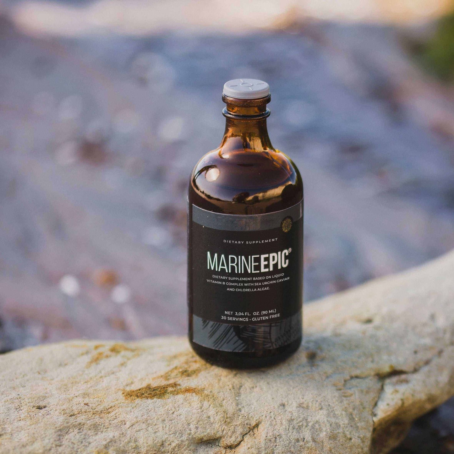 Brown glass bottle of Marine Epic biotechnology supplement for longevity and biohacking placed on a rock with blurred ocean background