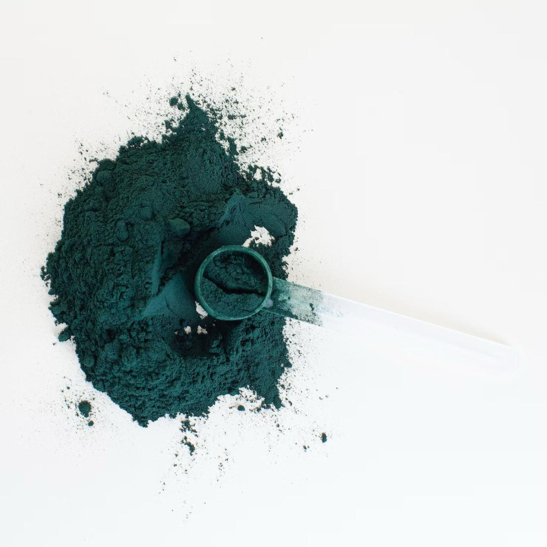 A scoop of spirulina with powder scattered in the background.